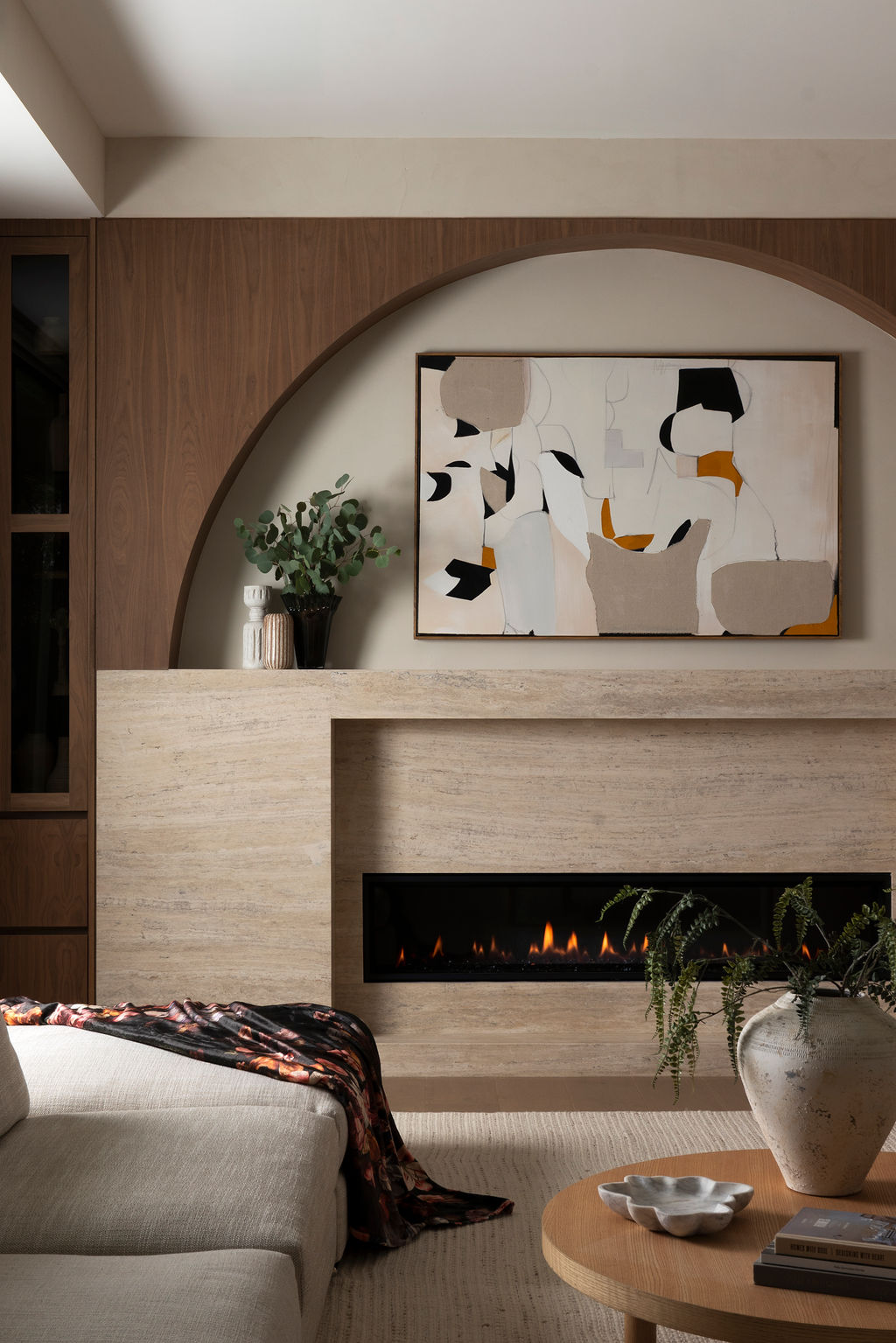 A living room with a pale stone fireplace, arched walnut surround, and abstract artwork